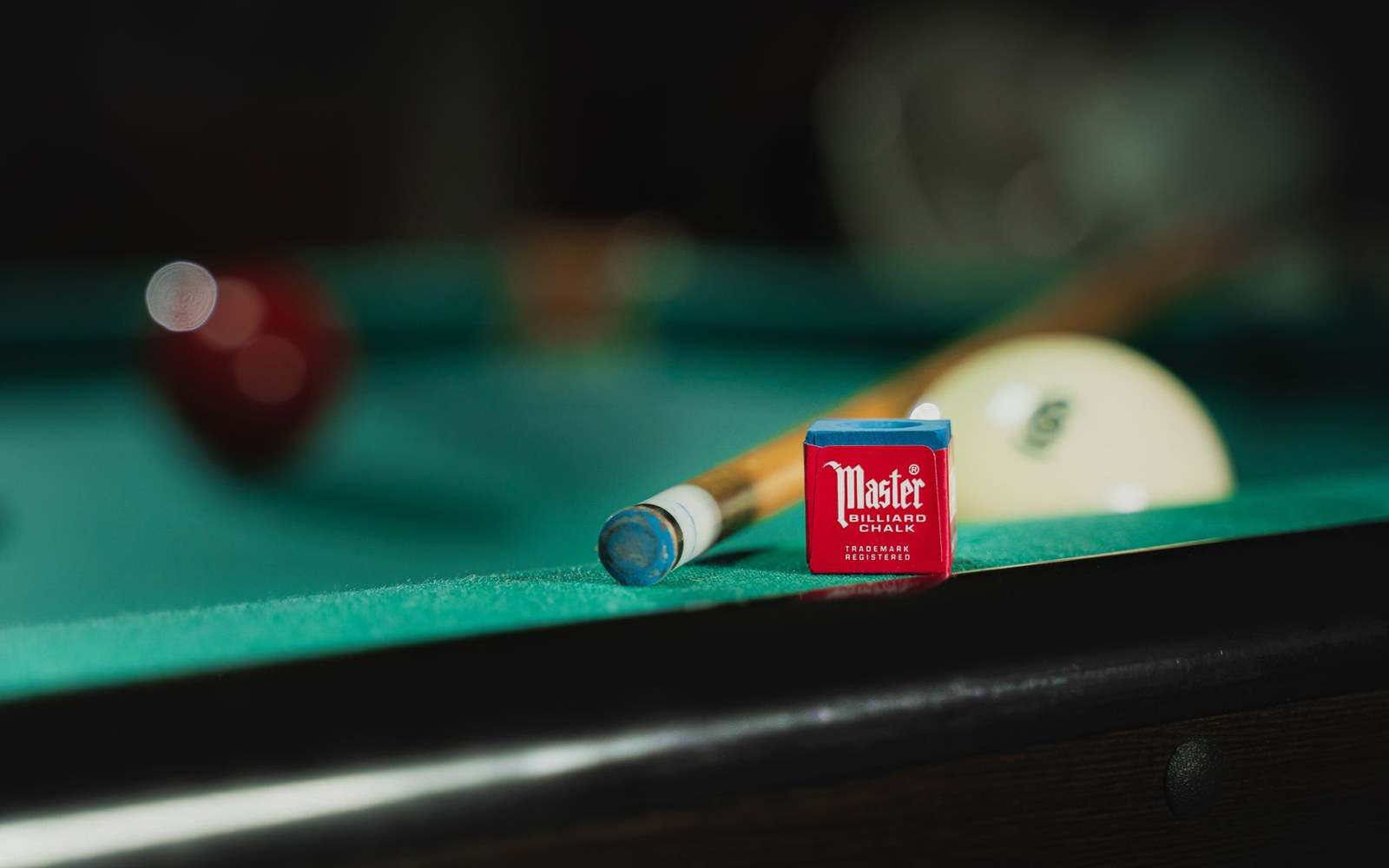 A piece of blue billiards chalk worn to a deep cup, resting on a snooker table cushion rail