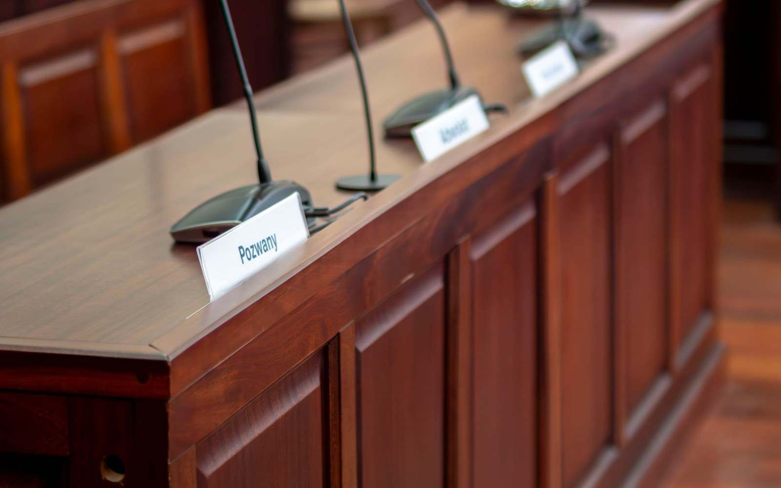 Wooden courtroom bench with microphones and a "Pozwany" nameplate for the defendant