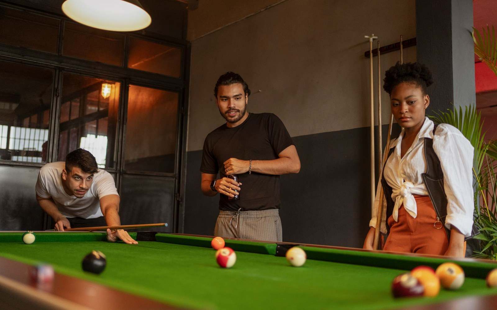 Three friends gather around a pool table as one lines up a shot