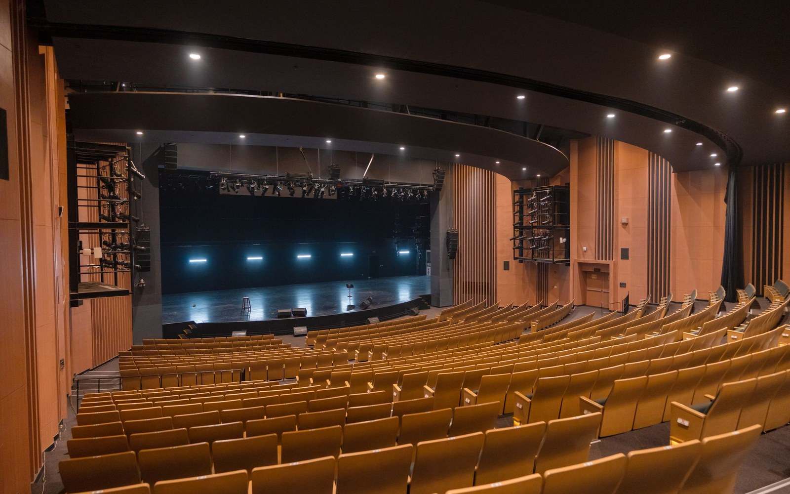 Empty theater auditorium with rows of wooden seats facing a bare, lit stage