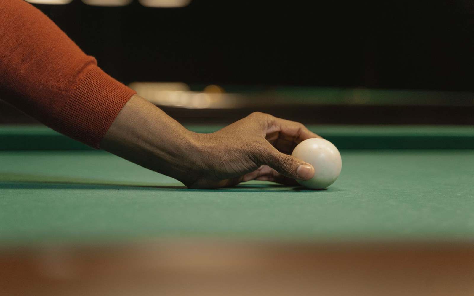 A hand places a white cue ball on the green felt of a pool table