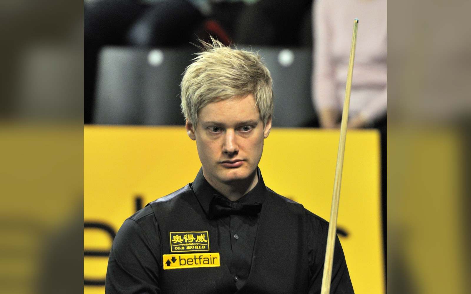 Snooker player in black waistcoat holds his cue while standing before a betfair backdrop