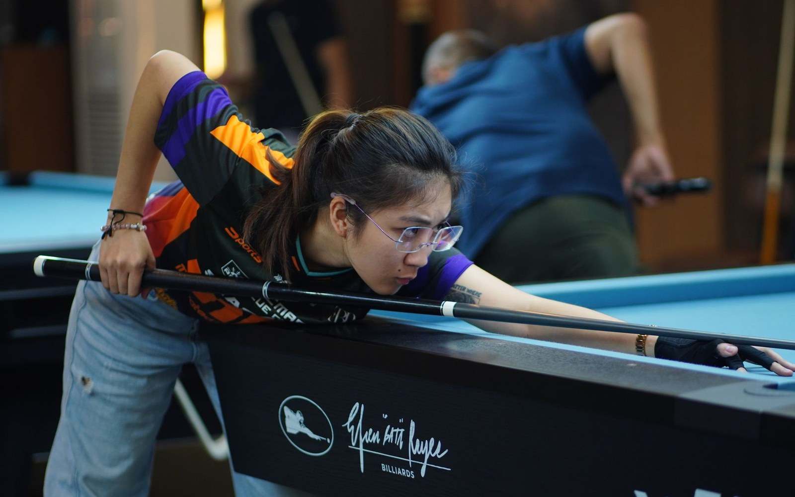 A female pool player leans over a billiard table, lining up a shot with her cue