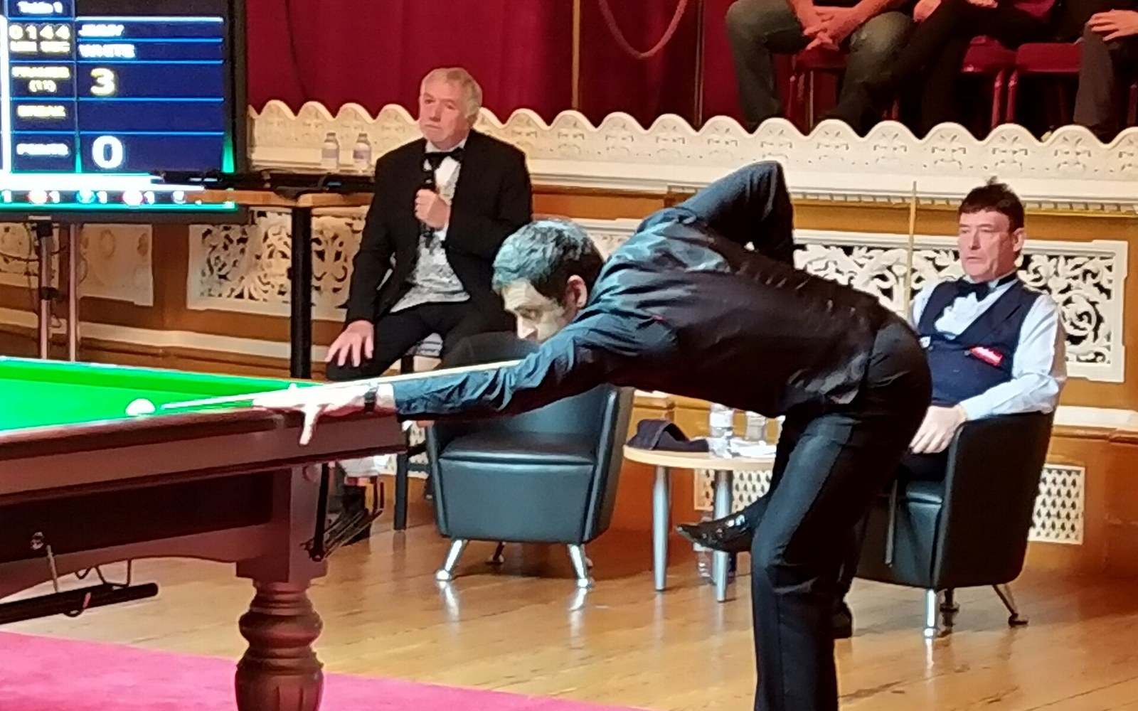Snooker player leans over the table to take a shot as referee and official look on