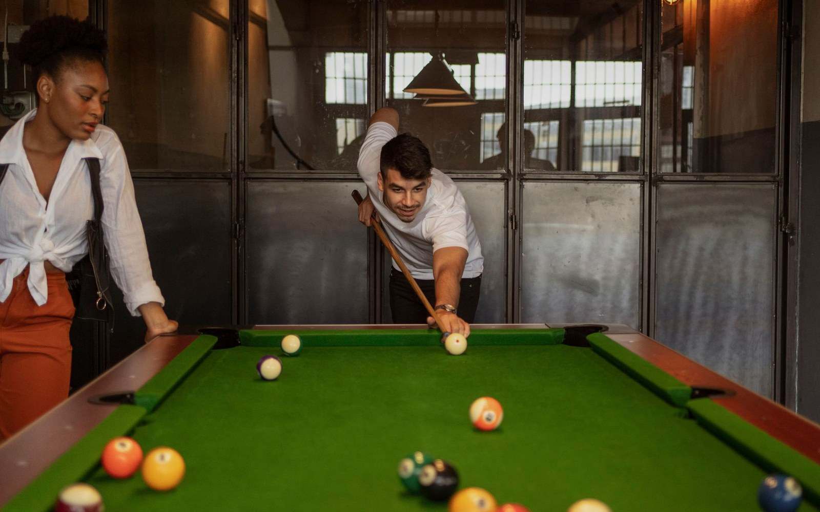 A man leans over a pool table to take a shot as a woman watches
