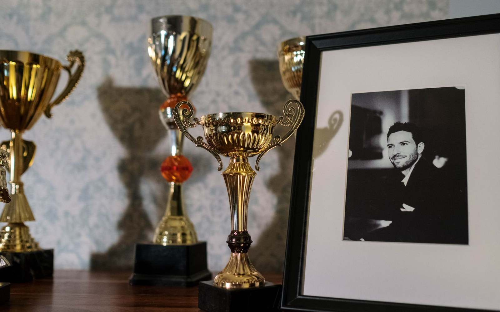 Gold trophies displayed beside a framed black-and-white photo of a smiling man