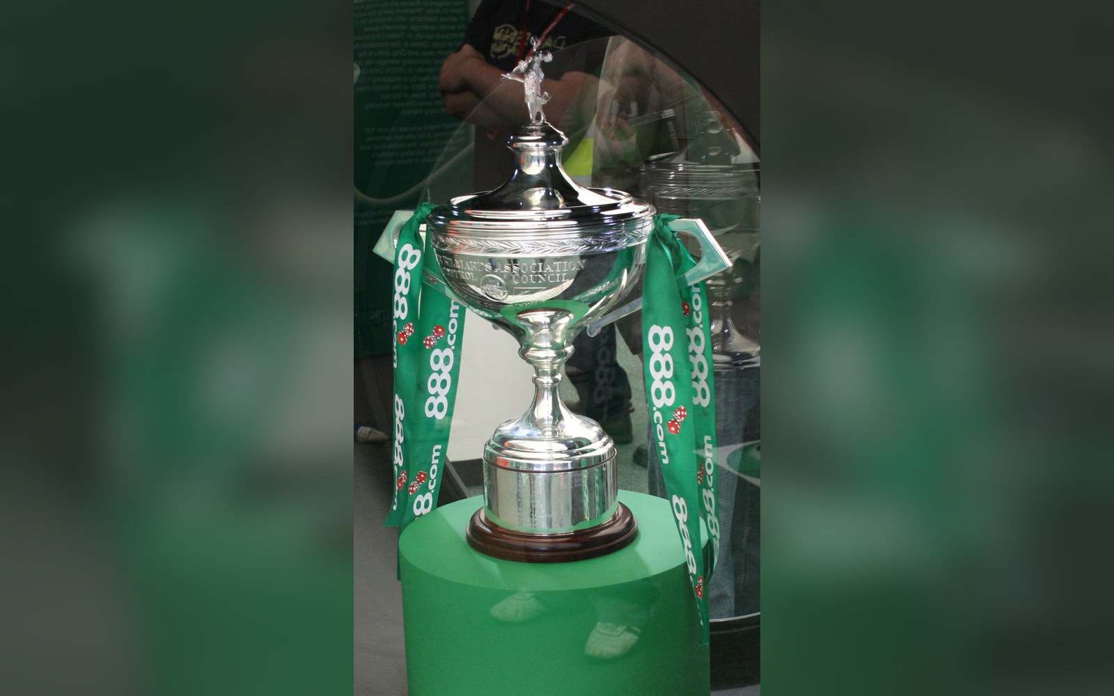 Silver snooker trophy on display, draped with a green sponsor ribbon