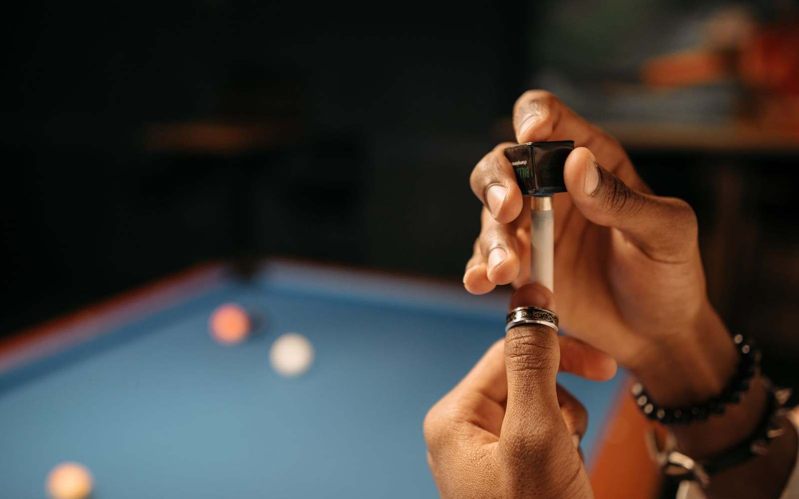 Close-up of hands applying chalk to a pool cue tip near a billiards table