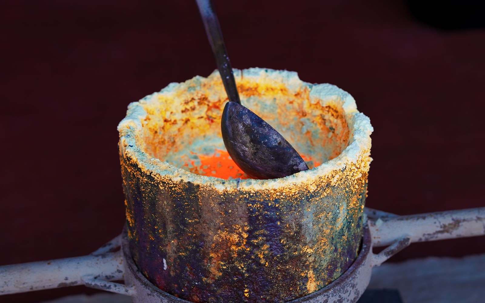 A metal ladle rests inside a crucible glowing with molten material during a casting process
