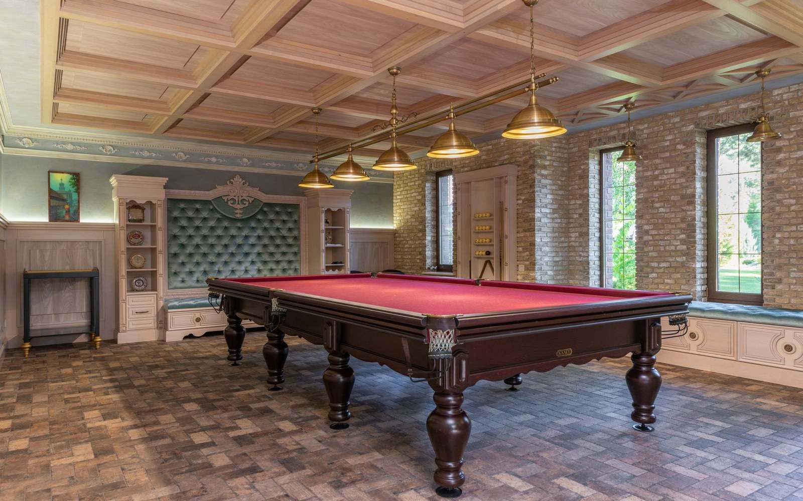 Long red felt billiards table in an ornate wood-paneled room with brass pendant lights