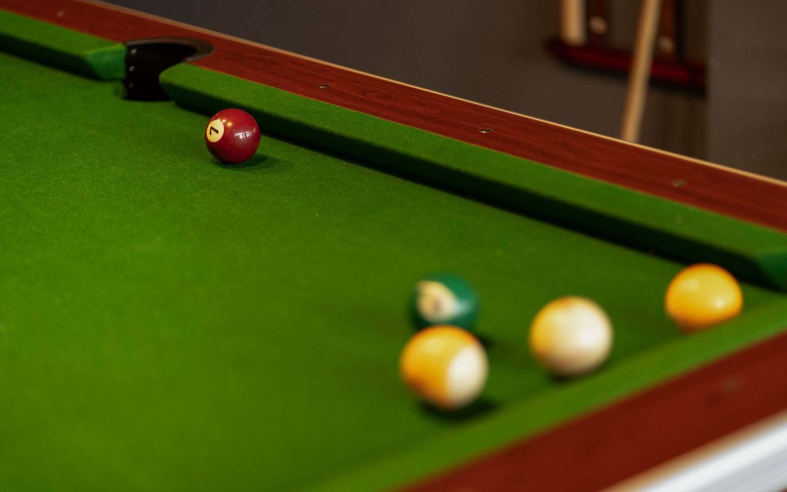 Billiard balls including a striped seven ball rest near a corner pocket on a green table