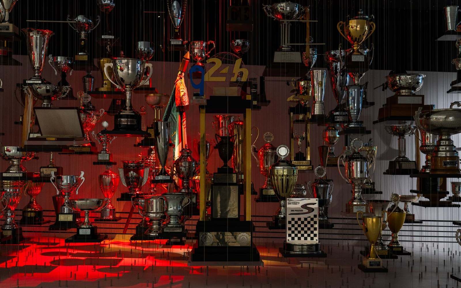 Rows of racing trophies and cups displayed under dramatic red lighting