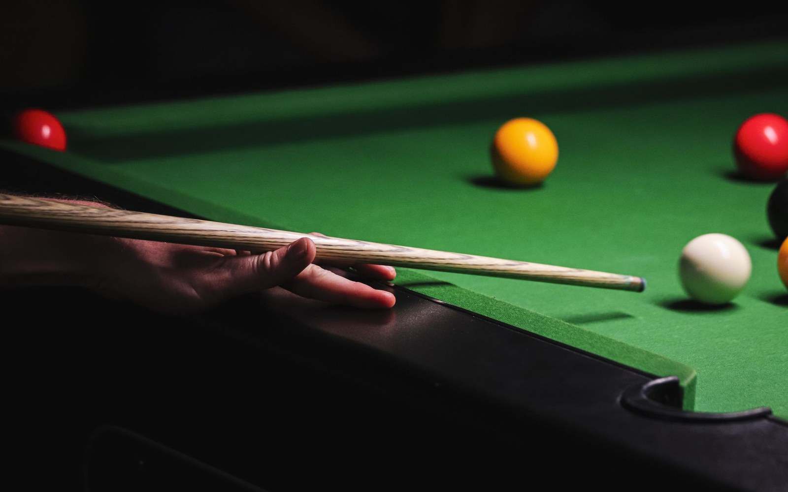 Close shot of a player's bridge hand spread over a snooker cushion, cue running through, mid-shot